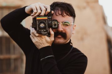 male photographer with big mustache taking photo with vintage camera